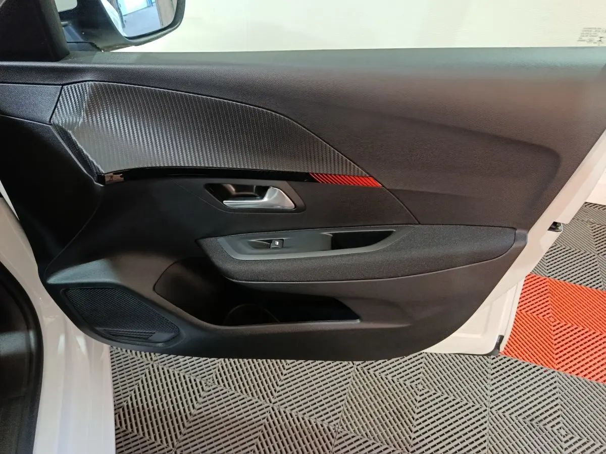 Vue intérieure côté gauche de la porte avant d'une Peugeot 208 électrique blanche avec insert décoratif noir et rouge.