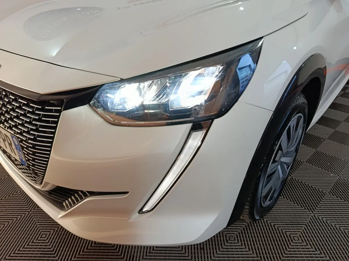 Gros plan sur l'avant droit blanc d'une Peugeot 208 électrique Active Business avec phares LED allumés.