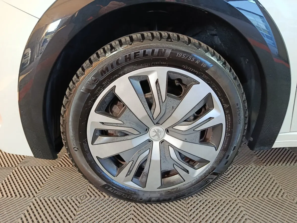 Gros plan sur la roue avant droite d'une Peugeot 208 électrique blanche, avec jante en alliage au design moderne.