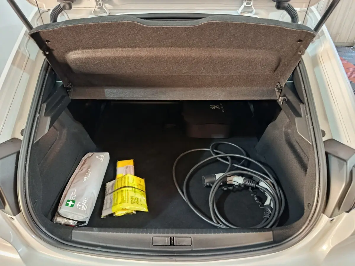 Coffre ouvert vu de dessus d’une Peugeot 208 Electrique Active Business blanche avec câble de recharge et kit de sécurité.