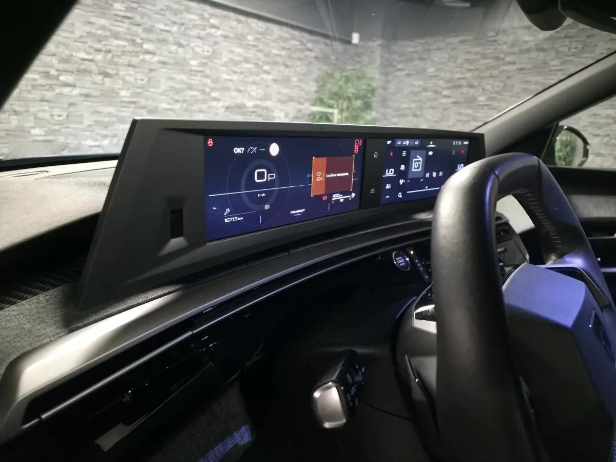 Vue intérieure du tableau de bord et volant noir du Peugeot 5008 hybride 2025 avec double écran panoramique HD flottant.