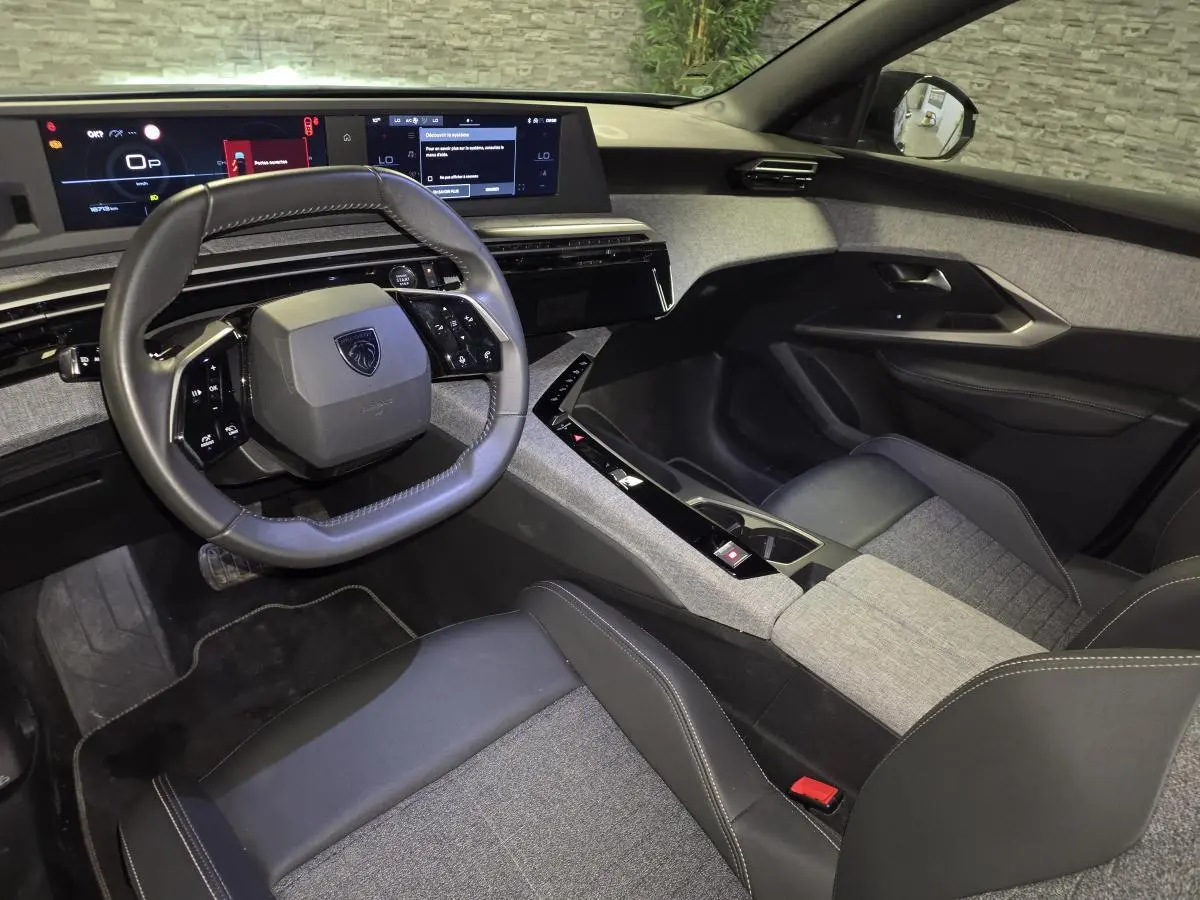 Intérieur avant droit du Peugeot 5008 2025 avec volant compact, sellerie tissu gris et cuir noir, et double écran HD panoramique.
