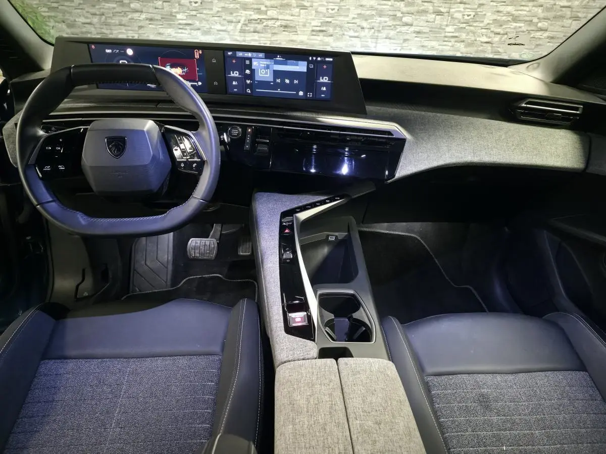 Vue intérieure avant du Peugeot 5008 2025, avec tableau de bord numérique, volant compact et sellerie tissu gris et noir.