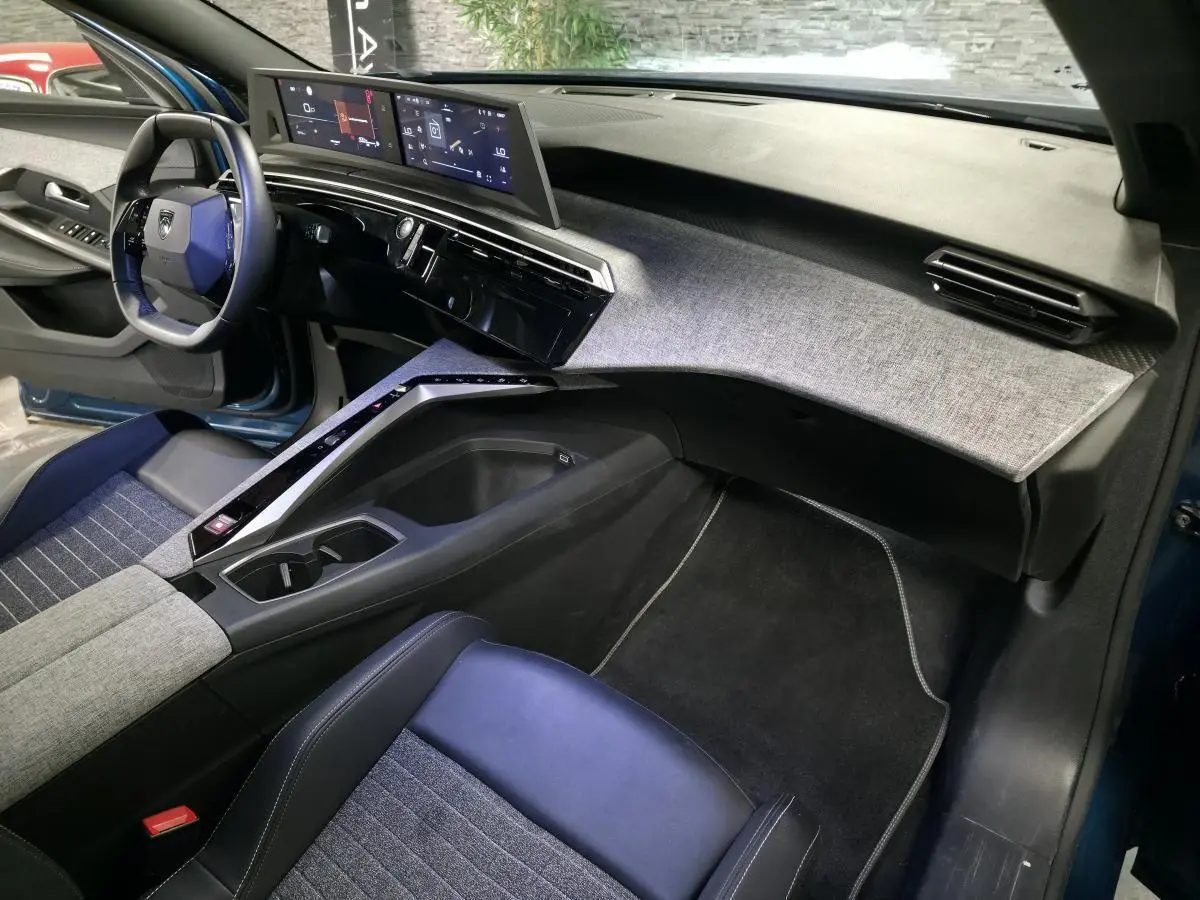 Intérieur avant droit du Peugeot 5008 bleu 2025, tableau de bord avec double écran HD et habillage tissu gris.