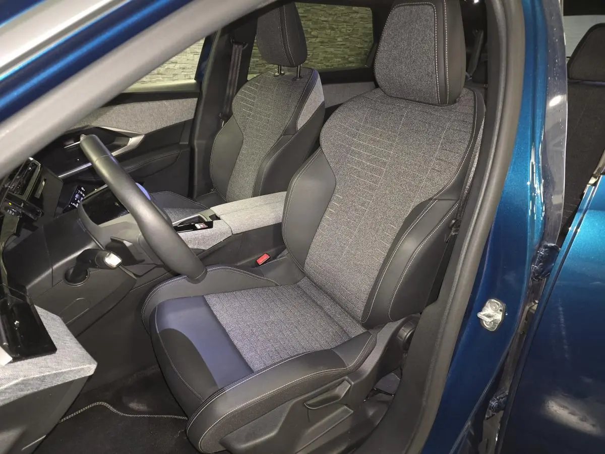 Vue intérieure côté conducteur du Peugeot 5008 bleu 2025, sièges tissu gris et cuir noir avec surpiqûres contrastées.