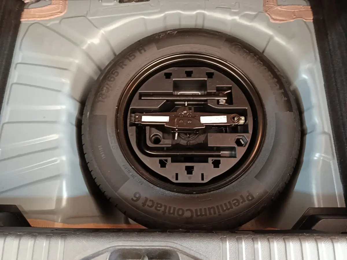 Vue plongeante sur la roue de secours et son kit d'outils dans le coffre d'une Renault Clio Business gris foncé.