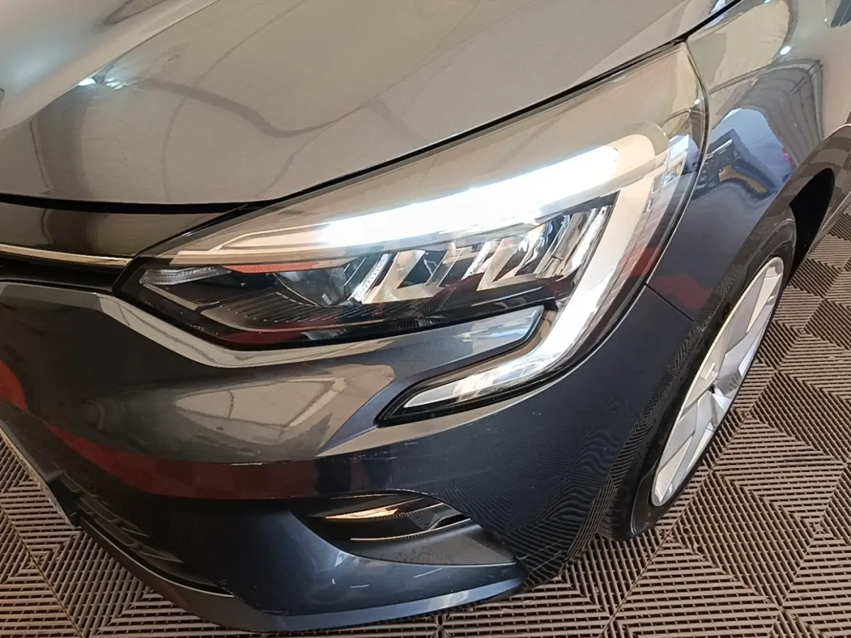 Gros plan sur l'avant droit gris foncé de la Renault Clio 2021 avec ses phares LED allumés et jante visible.