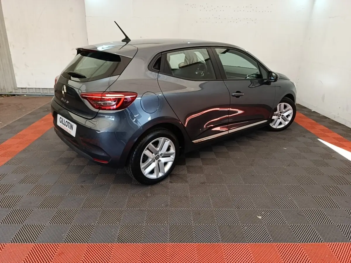 Renault Clio Business TCe 100 gris foncé vue 3/4 arrière droit dans un espace intérieur avec sol à damier noir et orange.