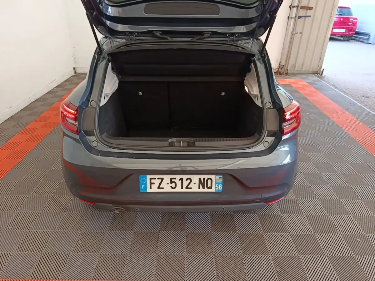 Vue arrière d'une Renault Clio Business TCe 100 gris foncé avec coffre ouvert dans un garage.