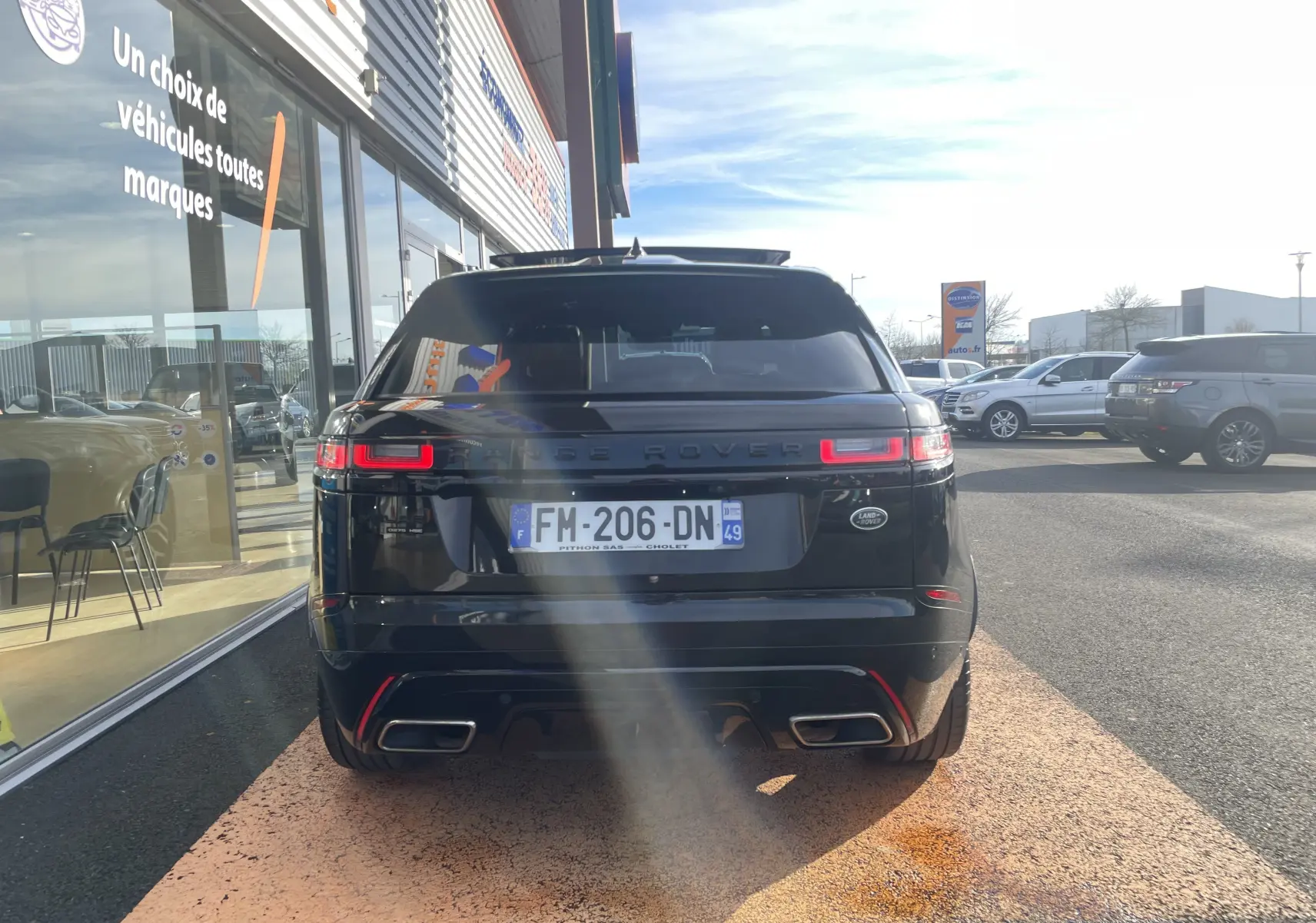 Vue arrière d'un Range Rover Velar noir Santorini garé devant un showroom, avec ses feux LED allumés.