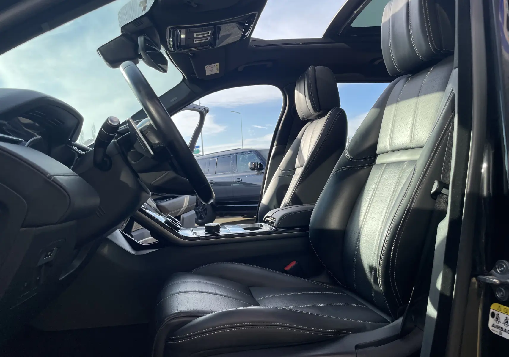 Intérieur du Range Rover Velar noir Santorini 2019, vue côté conducteur sur sièges cuir noirs et toit panoramique ouvert.