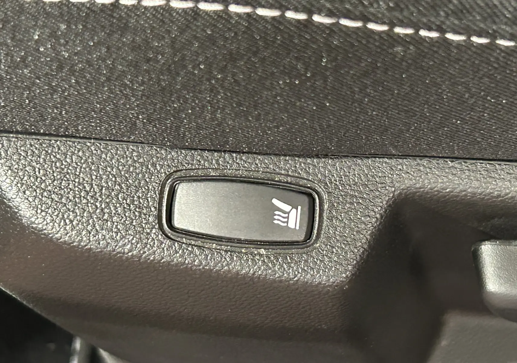 Bouton de siège chauffant en gros plan sur la garniture intérieure noire du Dacia Duster orange Arizona 2022.