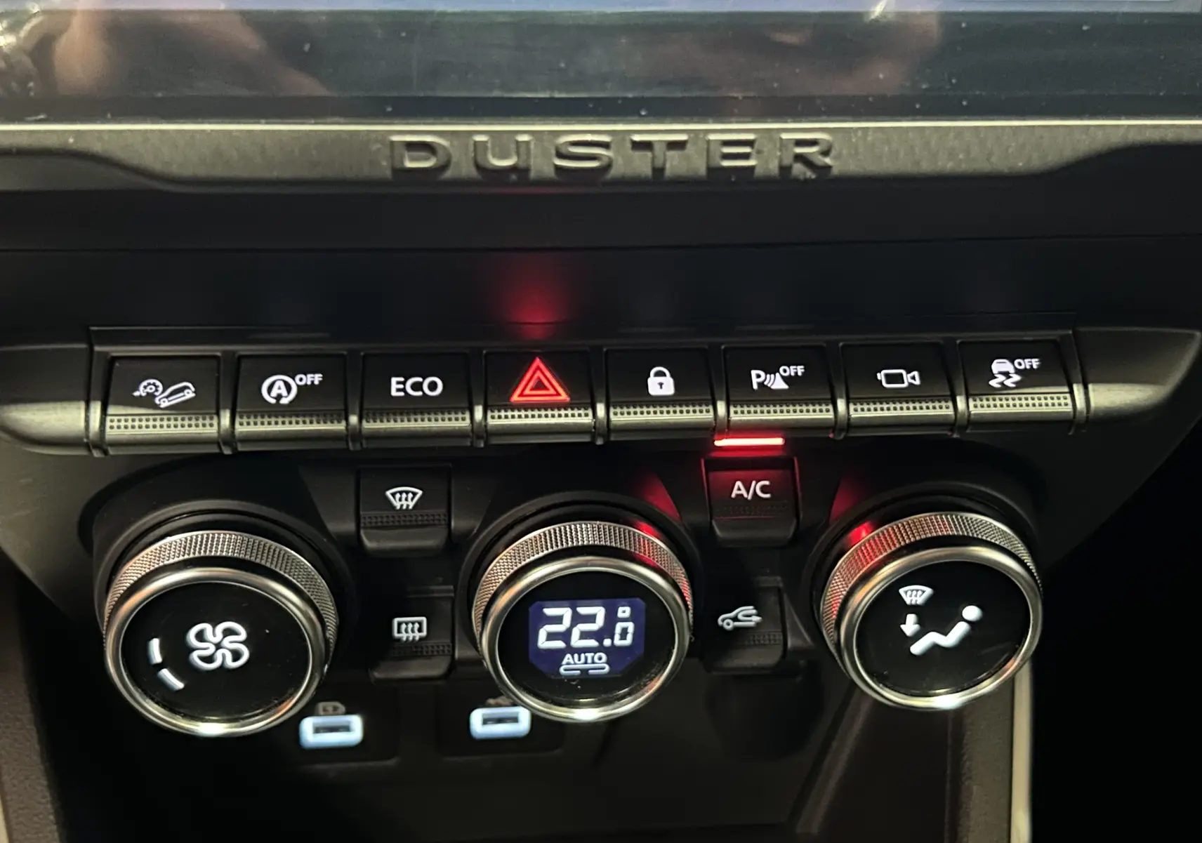 Gros plan sur la console centrale du Dacia Duster 2022 orange Arizona, montrant les commandes de climatisation et les boutons de fonction.