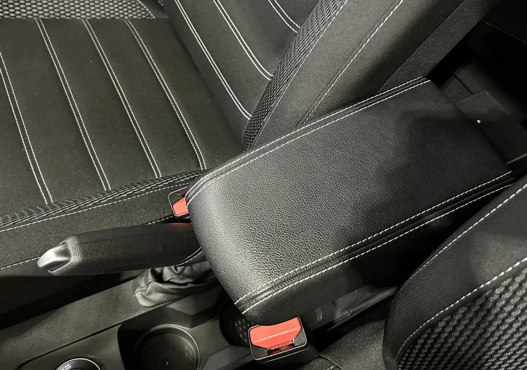 Gros plan sur l'accoudoir noir en cuir avec surpiqûres blanches entre les sièges avant en tissu noir à rayures blanches du Dacia Duster.