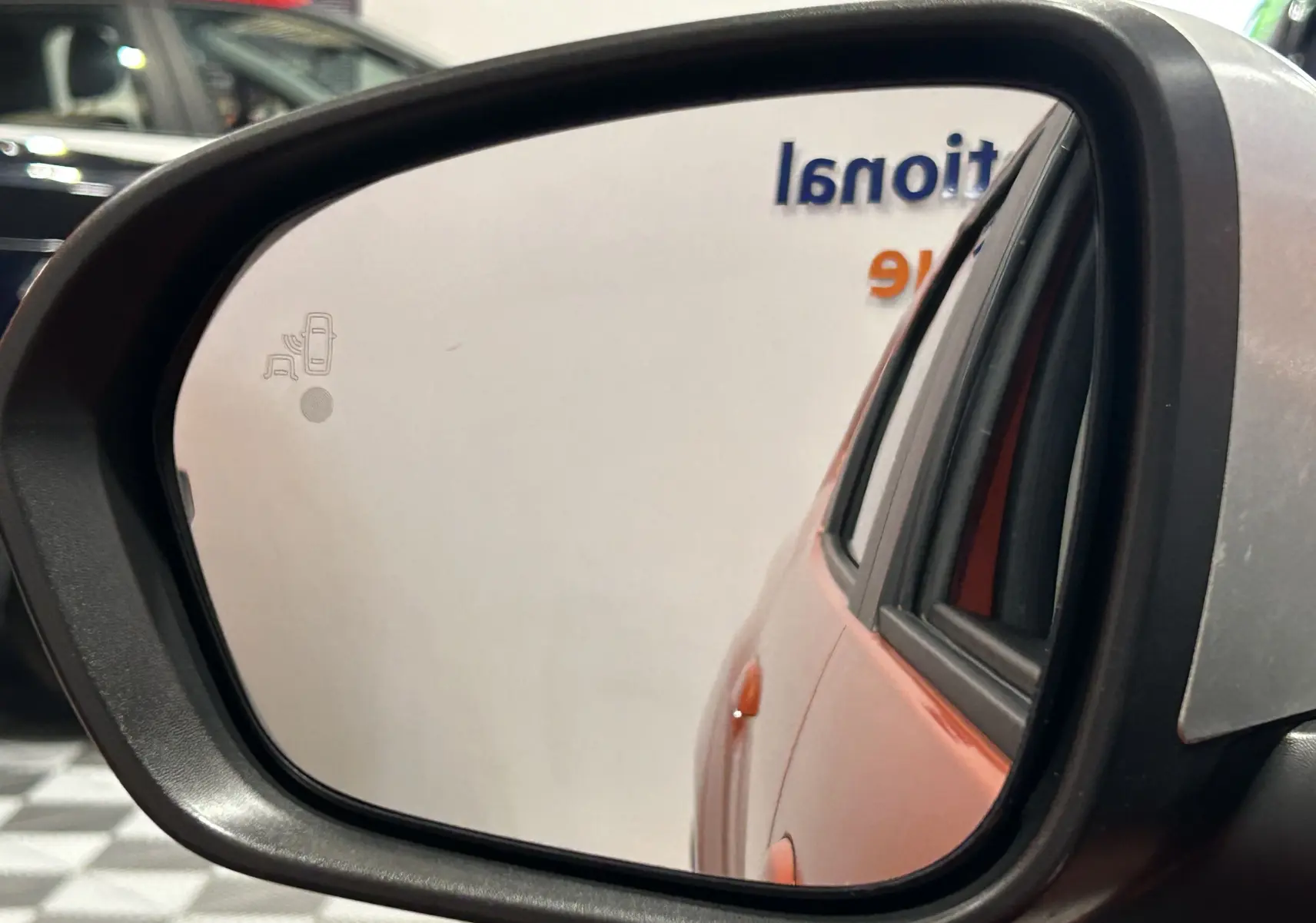 Reflet dans le rétroviseur gauche montrant la porte arrière orange Arizona du Dacia Duster 2022 avec caméra 360 et sièges chauffants.