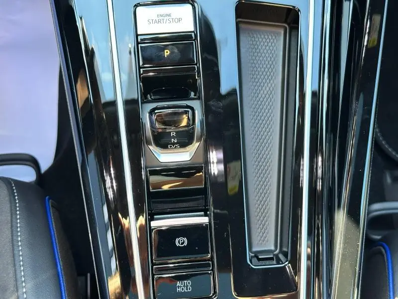 Vue rapprochée de la console centrale noire brillante de la Volkswagen Golf 2025, avec commandes boîte auto et frein électronique.