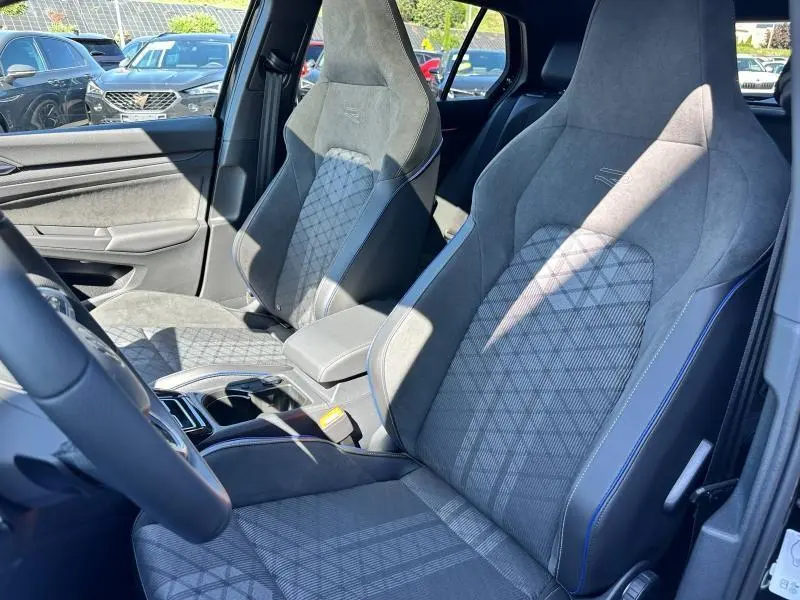 Intérieur de la Volkswagen Golf 1.5 eTSI R-Line 2025, vue côté conducteur, sièges sport en tissu gris avec surpiqûres bleues.