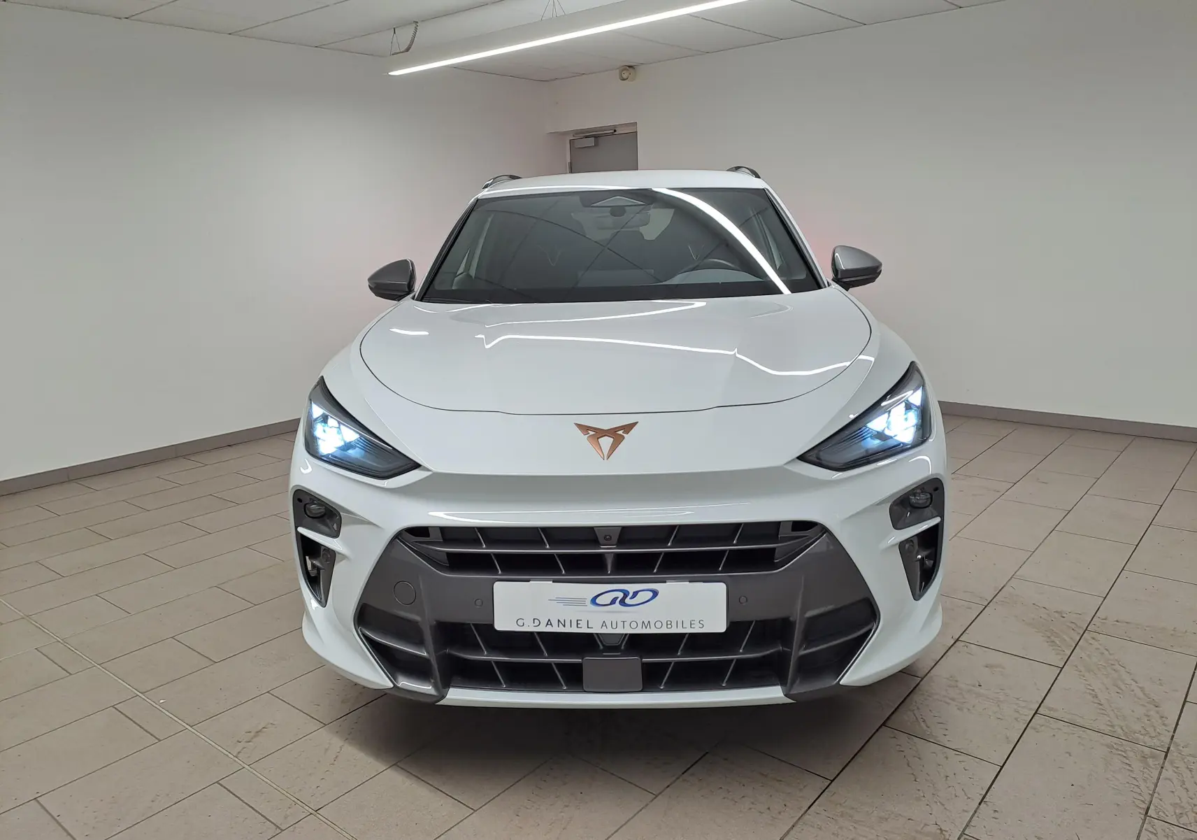 Vue frontale du CUPRA TERRAMAR blanc Nevada avec phares allumés et calandre noire distinctive.