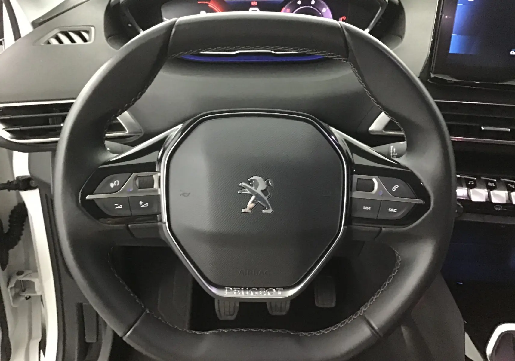 Vue rapprochée du volant cuir noir du Peugeot 5008 blanc nacré, avec commandes intégrées et tableau de bord numérique.