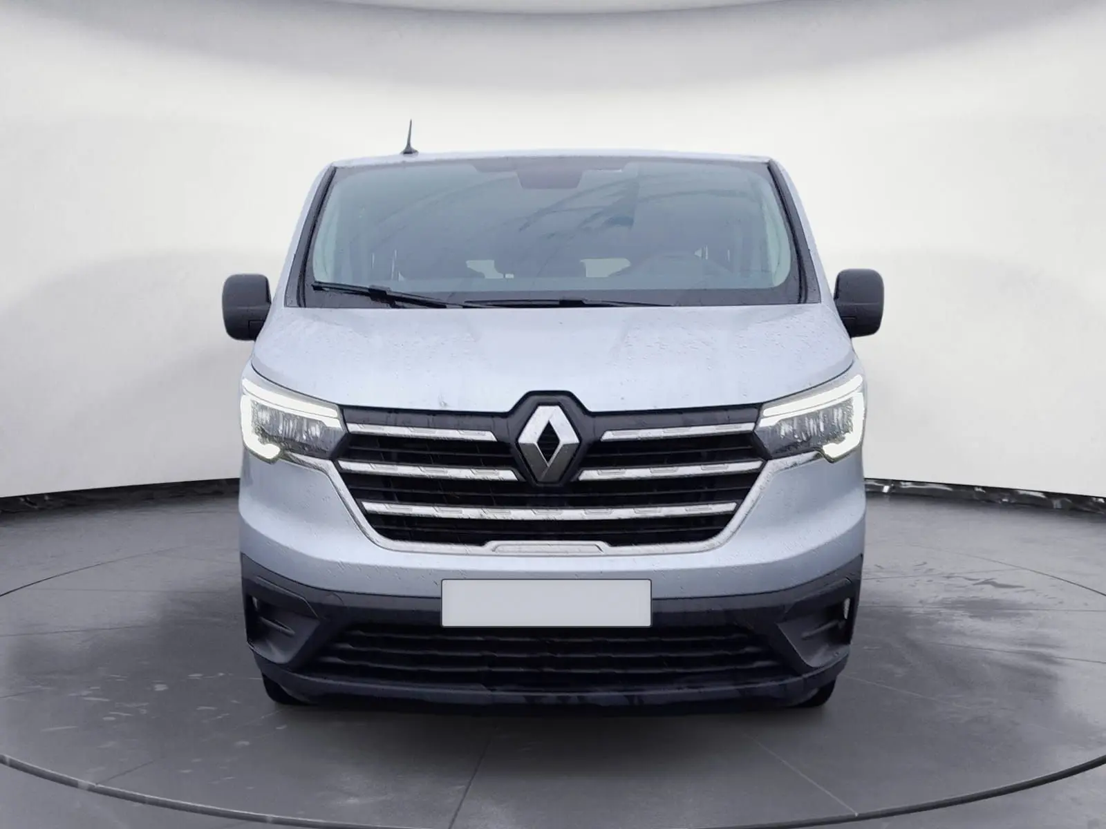 Vue frontale d'un Renault Trafic Combi gris clair métal 2023 avec calandre noire et phares allumés.