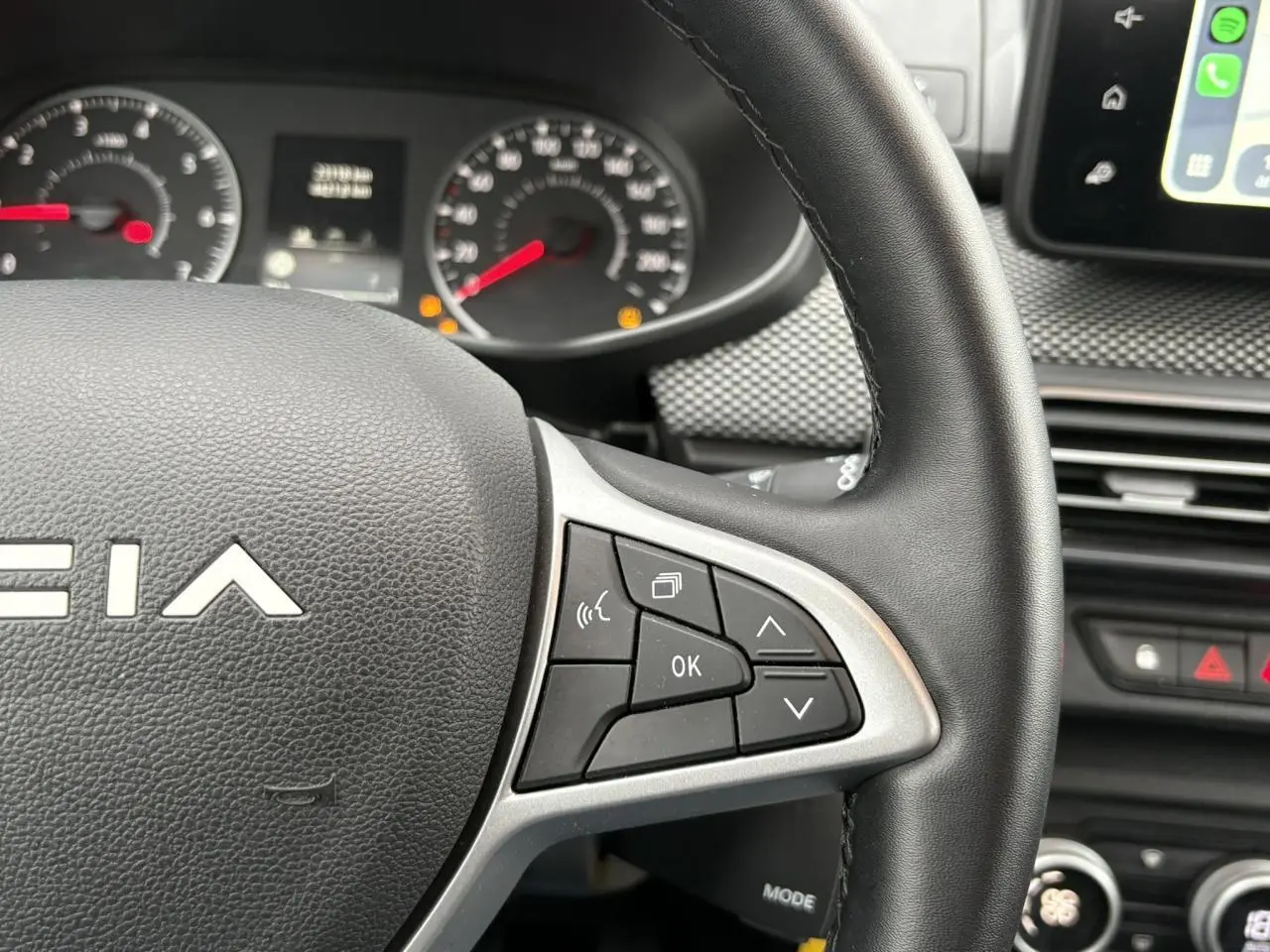 Gros plan sur le volant à droite avec commandes multifonctions du Dacia Jogger 2025, intérieur noir et tableau de bord visible.