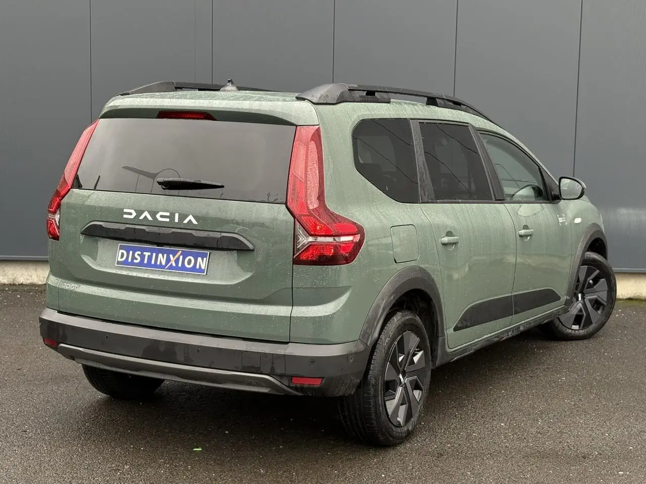 Vue 3/4 arrière droite d'un Dacia Jogger 2025 kaki lichen avec barres de toit et jantes spécifiques.