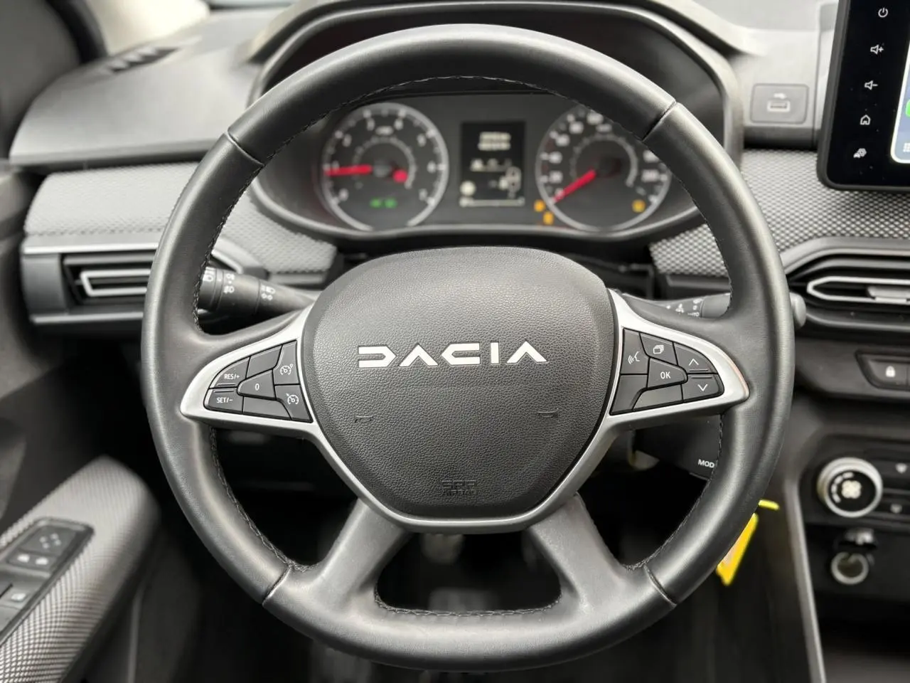 Vue rapprochée du volant noir de la Dacia Jogger 2025 avec tableau de bord et commandes au volant visibles.