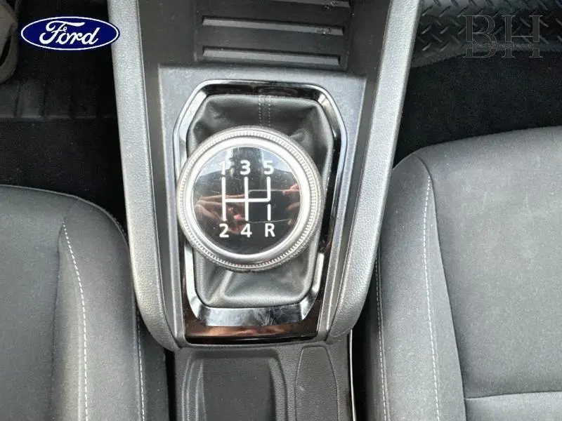 Vue en plongée sur le levier de vitesses manuel noir et les sièges tissu noir de la Renault Clio blanche 2020.