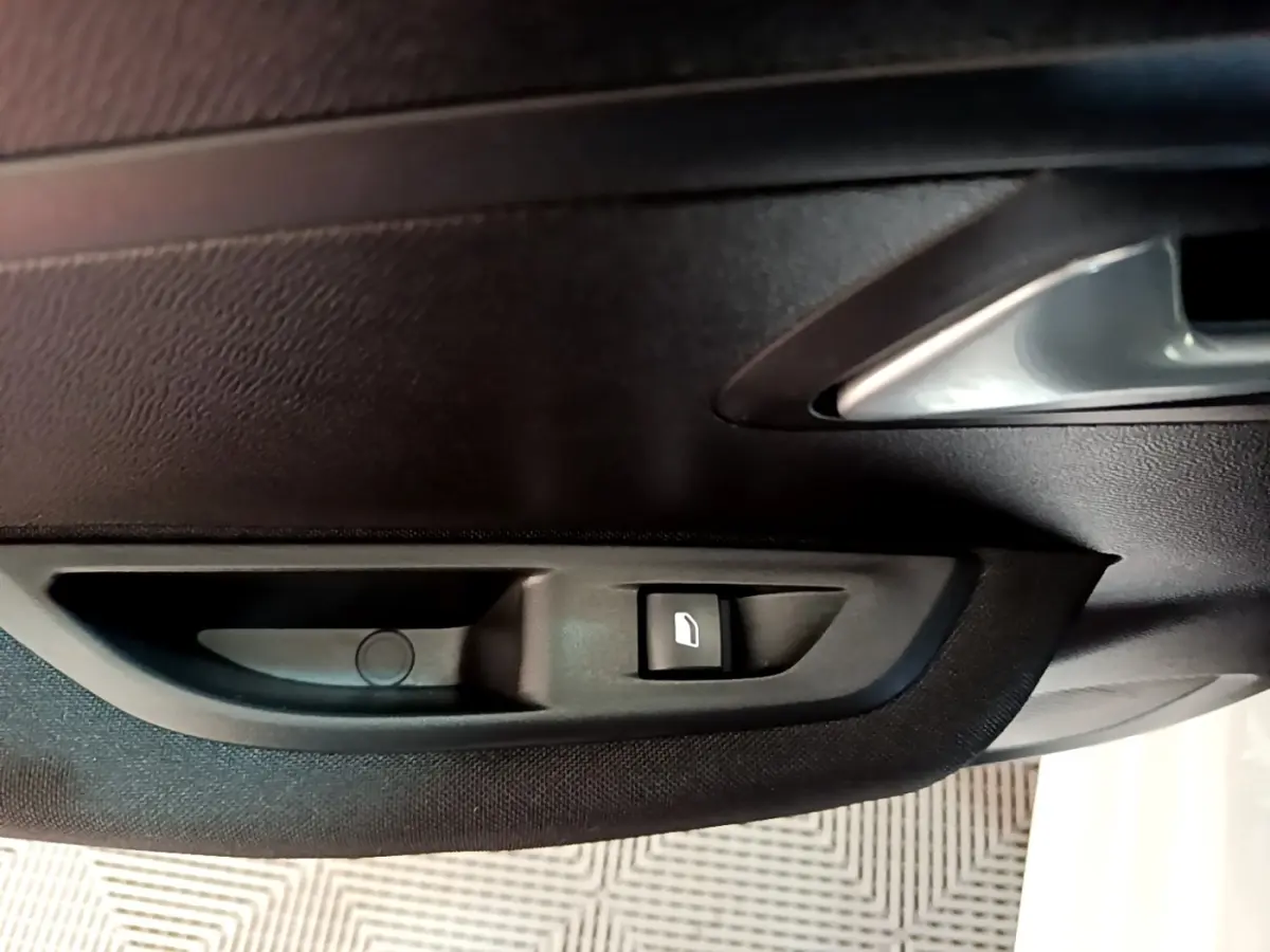 Gros plan sur la poignée intérieure et le bouton de lève-vitre côté conducteur d’une Peugeot 208 électrique blanche.