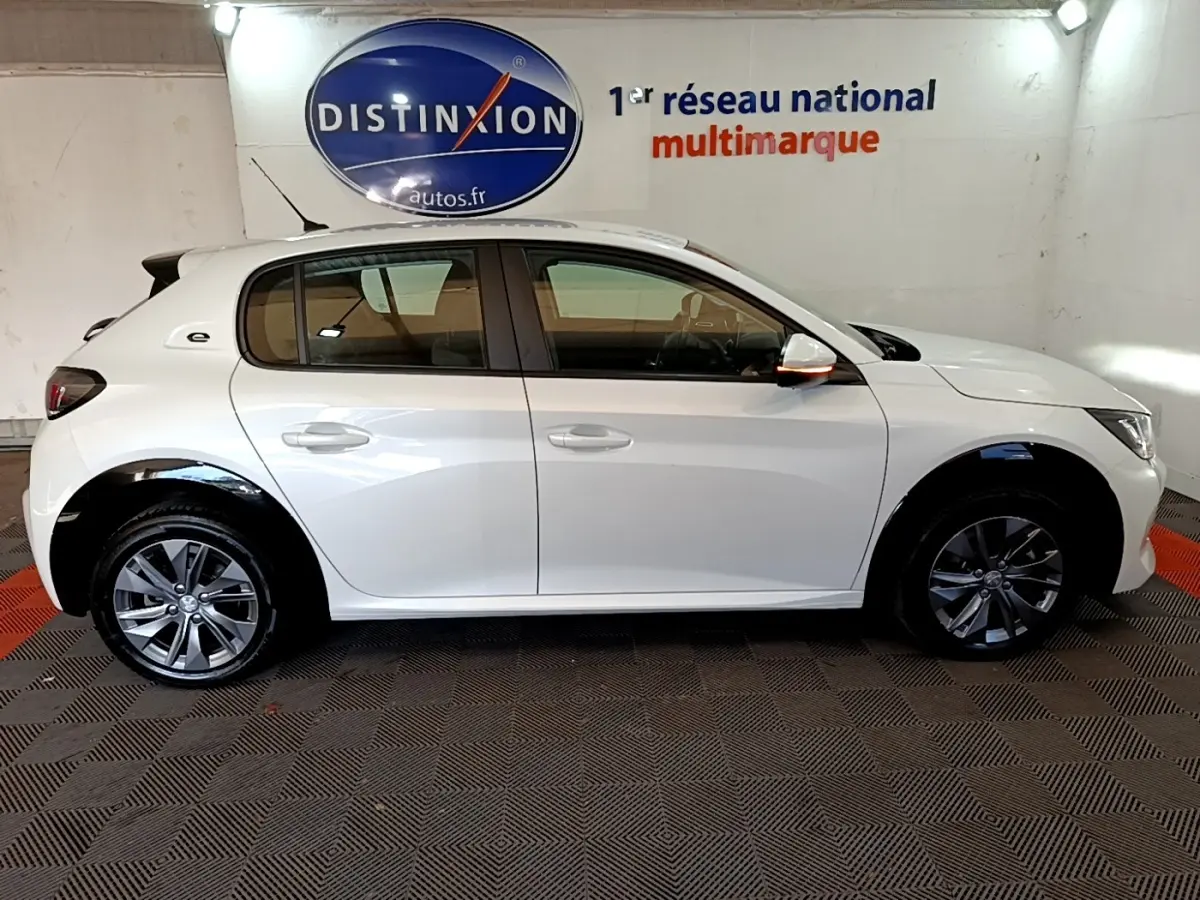 Vue de profil côté gauche d’une Peugeot 208 Electrique Active Business blanche en intérieur, avec jantes alliage et rétroviseurs blancs.