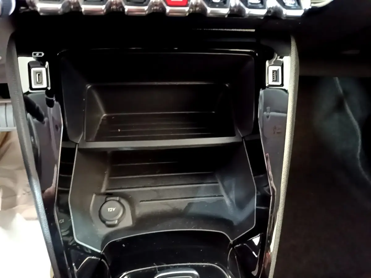 Vue rapprochée de la console centrale noire du Peugeot 208 électrique avec prise 12V et ports USB visibles.
