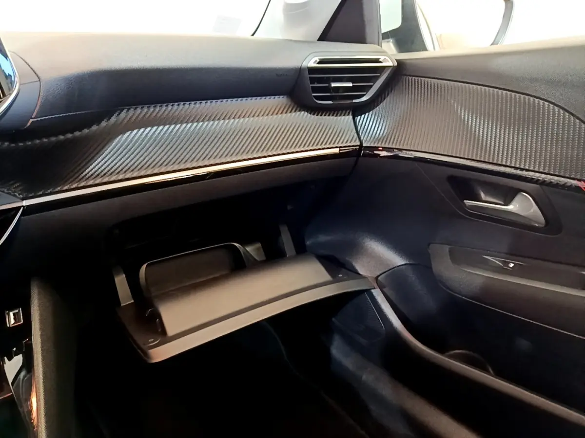 Vue intérieure côté passager du tableau de bord noir et boîte à gants ouverte d'une Peugeot 208 Electrique blanche.