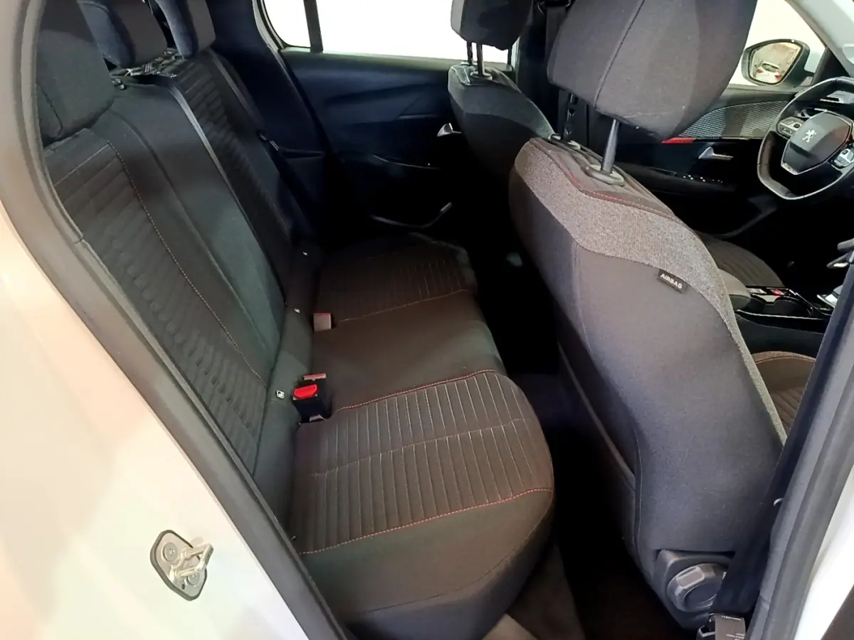 Vue intérieure côté arrière gauche du Peugeot 208 Electrique Active Business blanc, sièges tissu noir avec surpiqûres rouges.