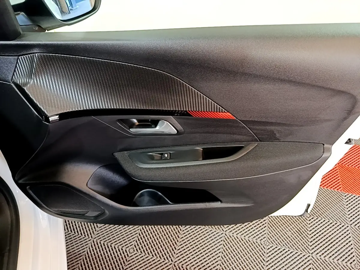 Vue intérieure côté gauche de la porte avant blanche du Peugeot 208 électrique avec insert carbone et détail rouge.