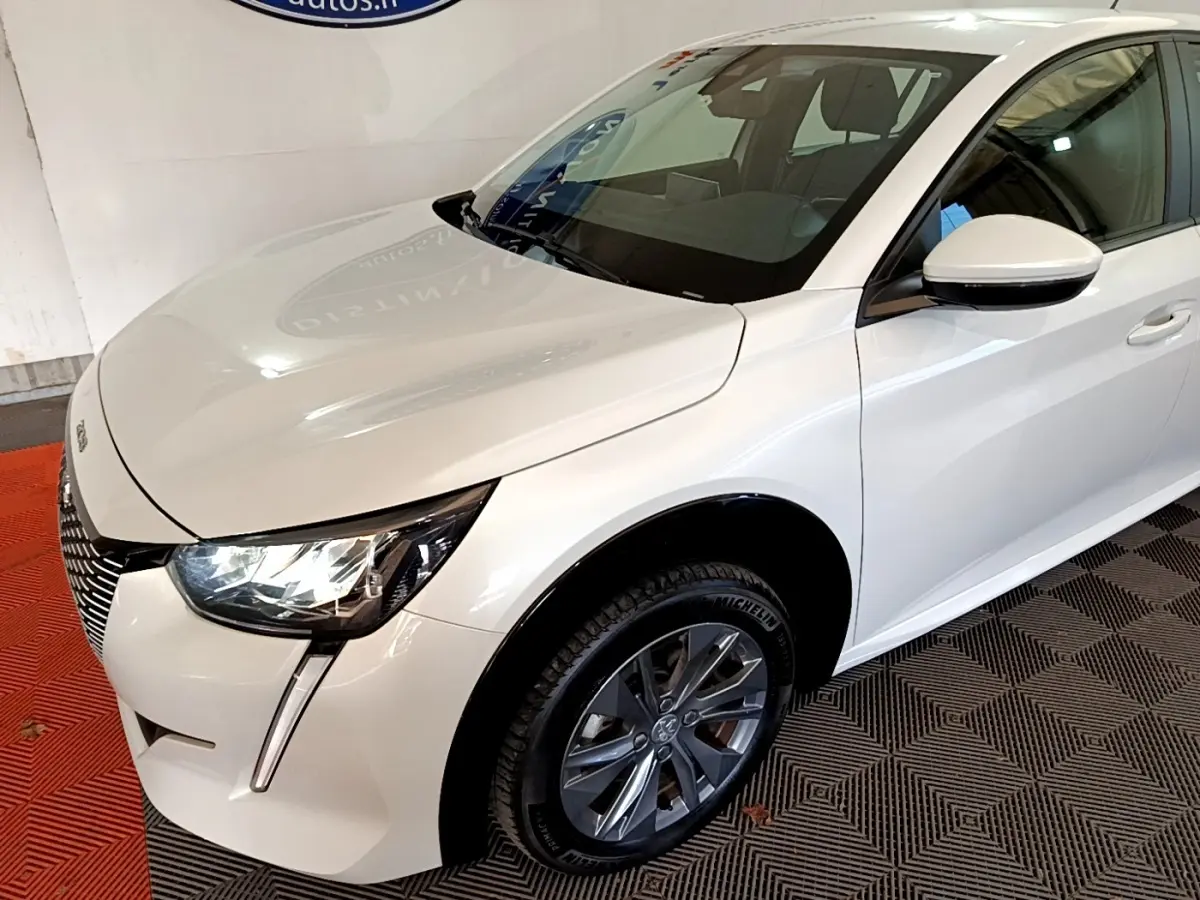 Vue 3/4 avant droite d'une Peugeot 208 électrique Active Business blanche avec phares LED et jantes alliage gris foncé.