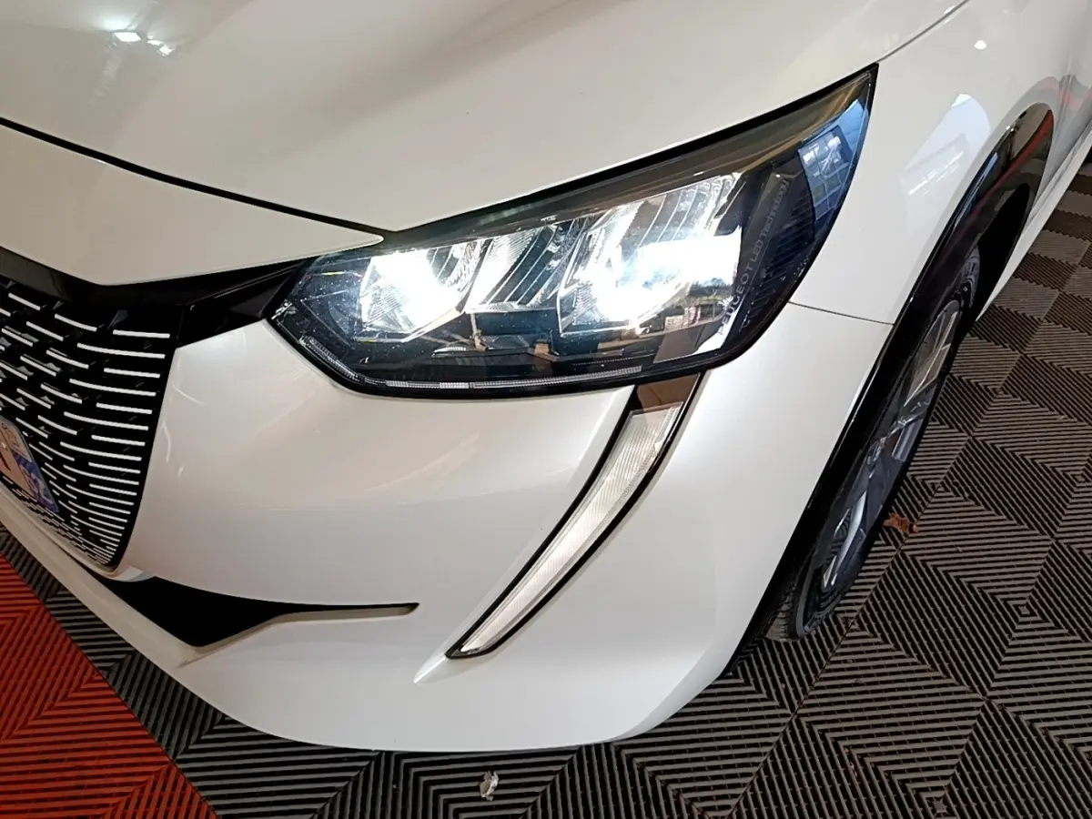 Gros plan sur l’avant droit blanc d’une Peugeot 208 électrique 2021, mettant en valeur le phare LED et la calandre distinctive.