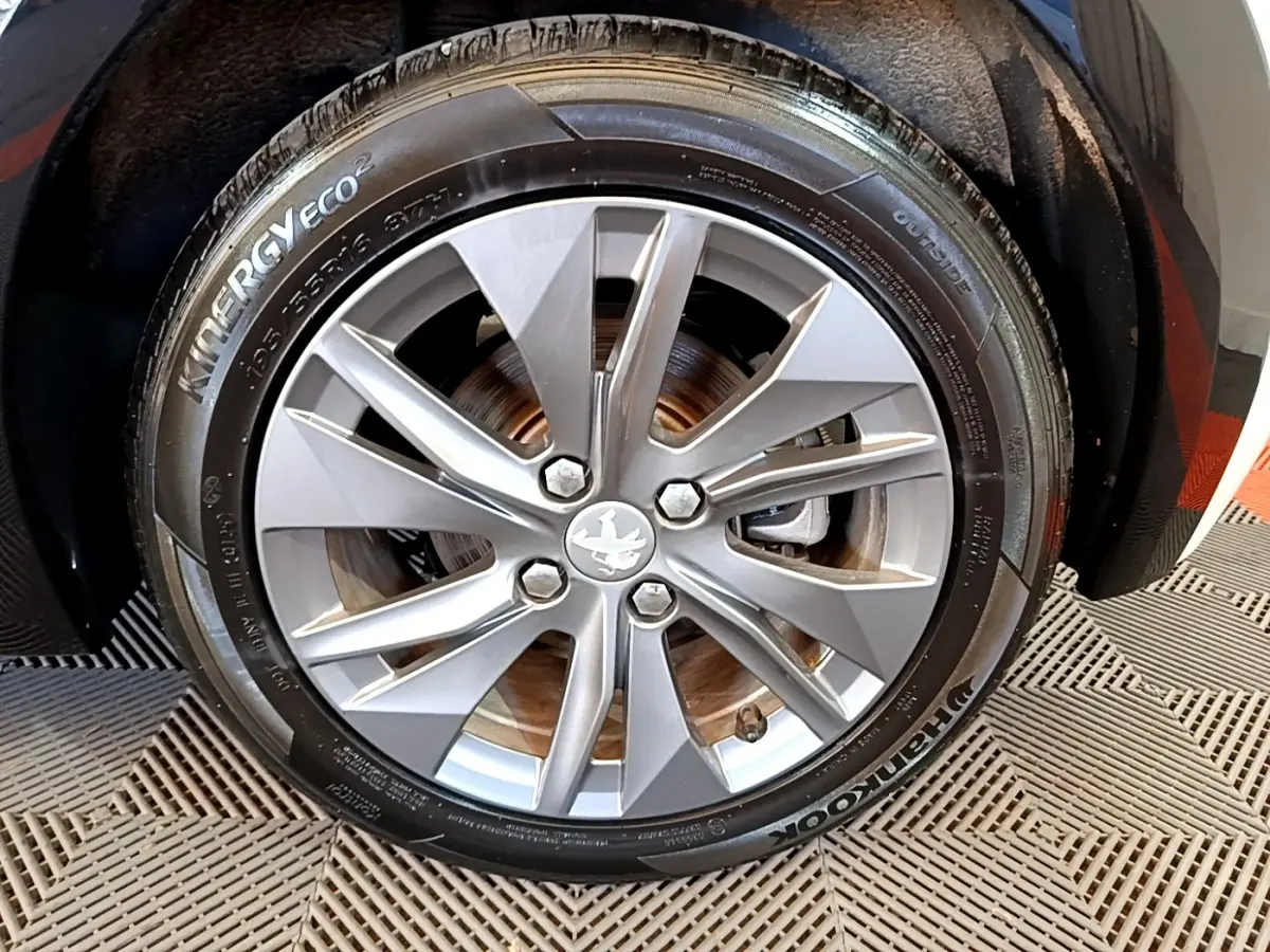 Gros plan sur la roue avant droite avec jante argentée et pneu Hankook d'une Peugeot 208 blanche électrique.