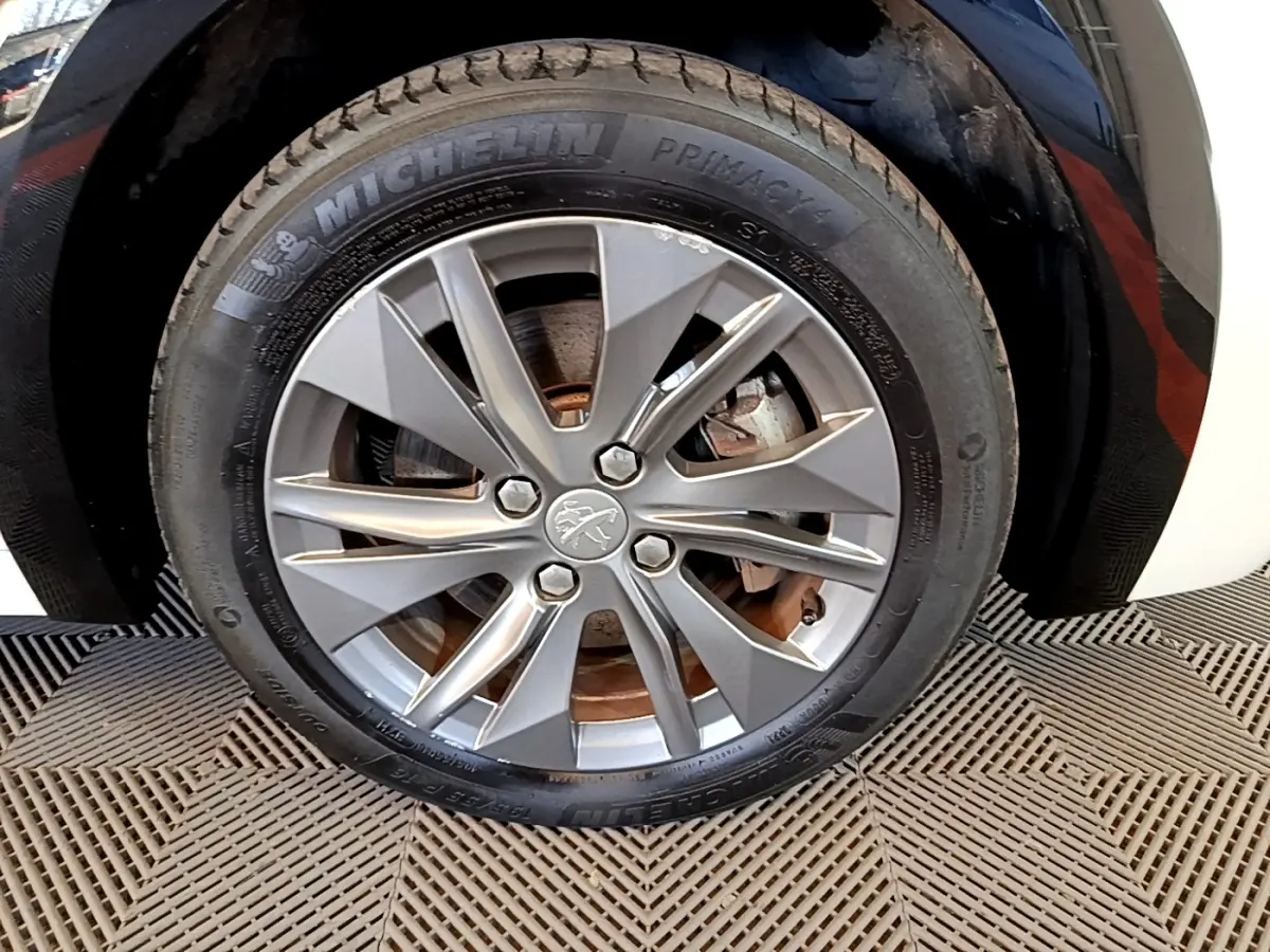 Gros plan sur la roue avant droite de la Peugeot 208 électrique blanche, jante alliage gris à 10 branches.