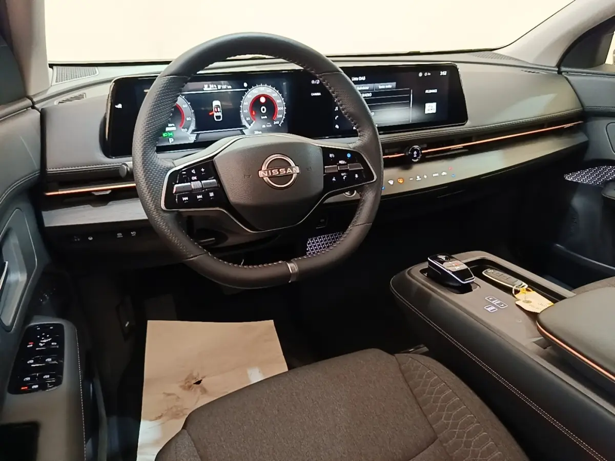 Vue intérieure avant du Nissan Ariya 63kWh noir, avec volant cuir multifonctions et grand écran tactile panoramique.