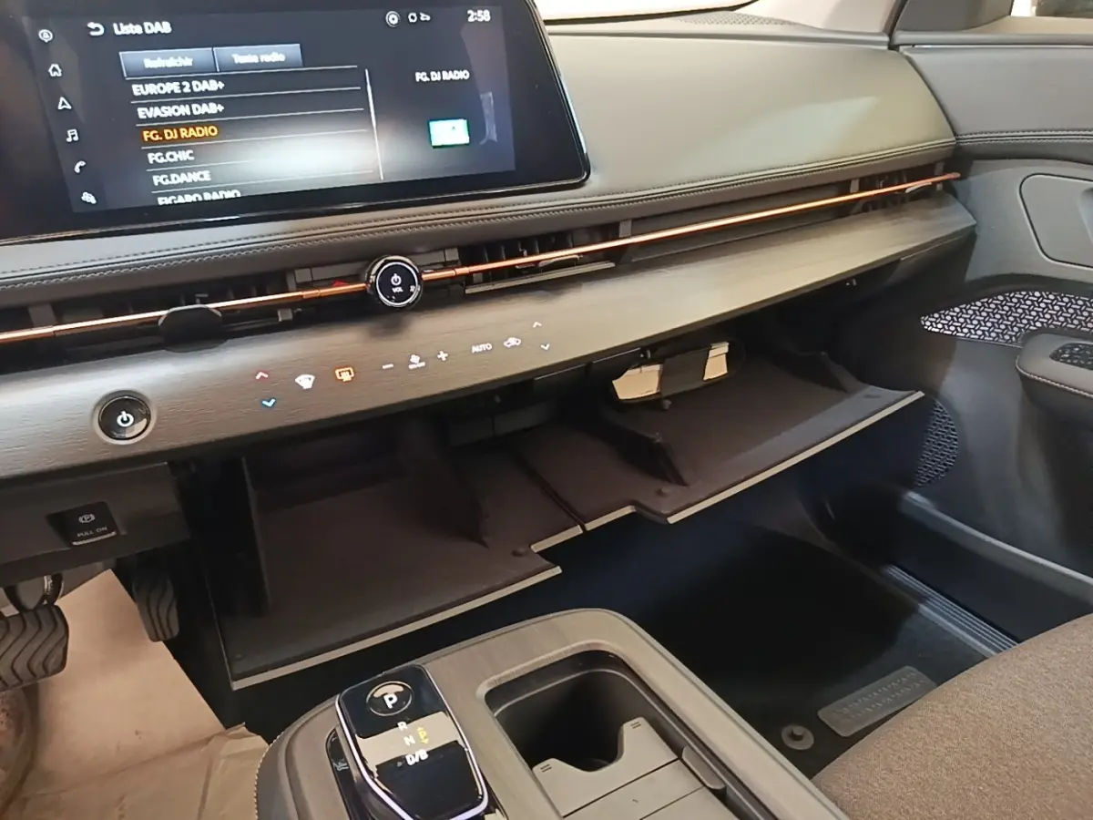 Vue intérieure côté passager du tableau de bord et boîte à gants ouverte du Nissan Ariya noir 2026 avec écran tactile.