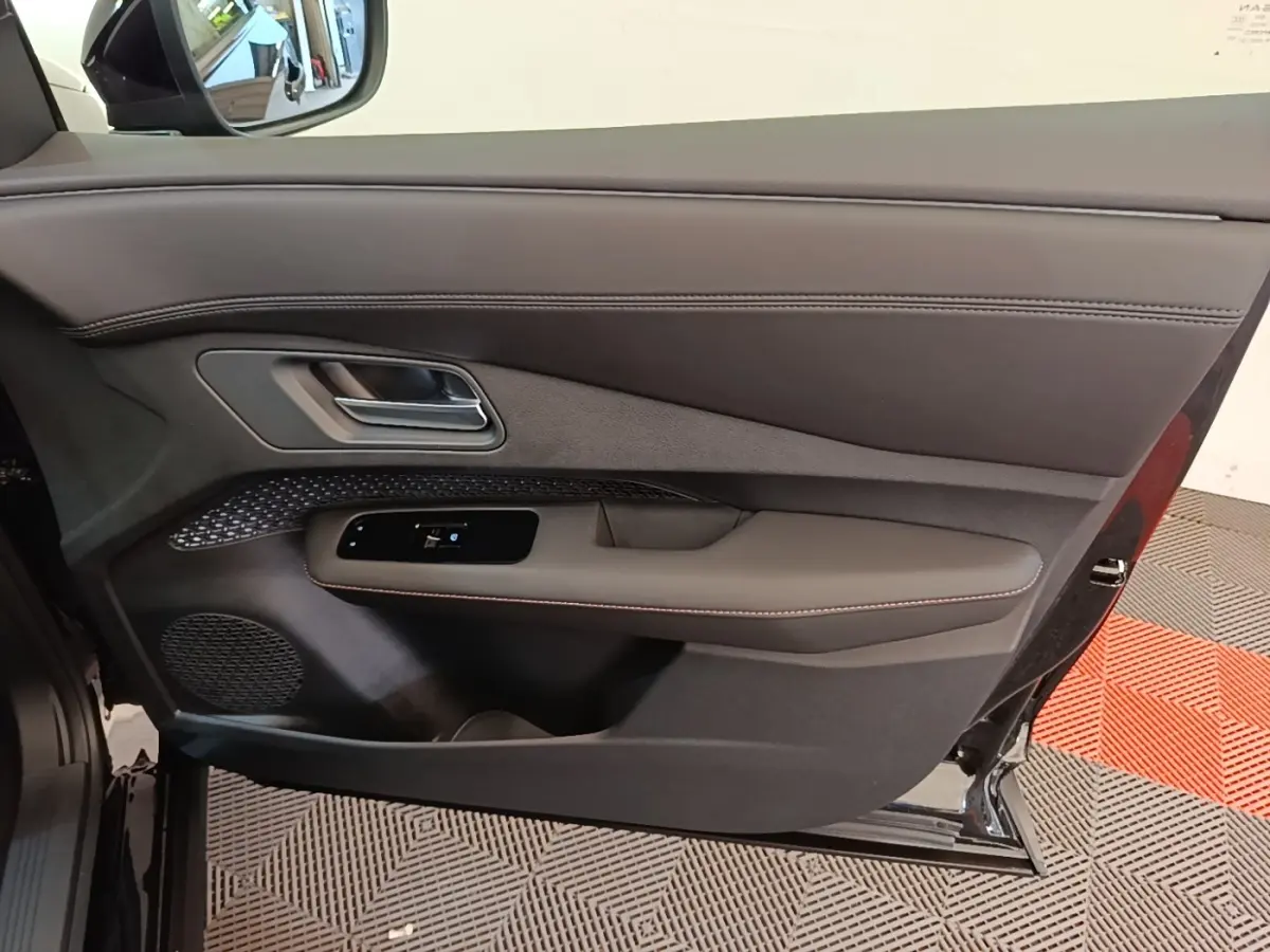 Vue intérieure côté gauche de la porte avant noire du Nissan Ariya 63kWh avec garniture cuir et commande vitres.