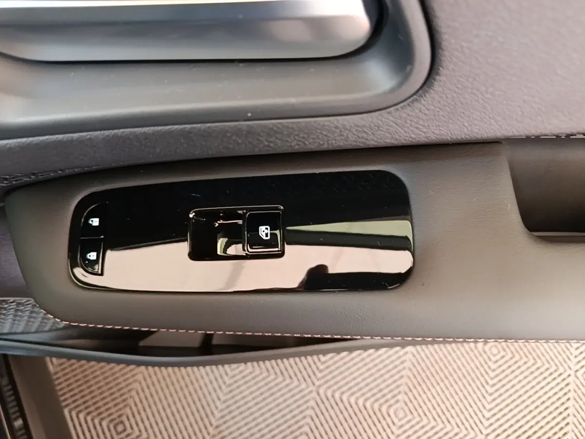 Gros plan sur la commande de lève-vitre côté conducteur du Nissan Ariya noir, avec finition brillante et surpiqûres rouges.
