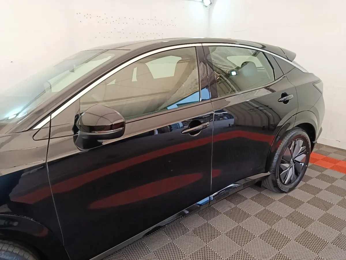 Vue latérale côté gauche d'un Nissan Ariya noir 63kWh 218ch Engage avec jantes modernes et rétroviseur assorti.