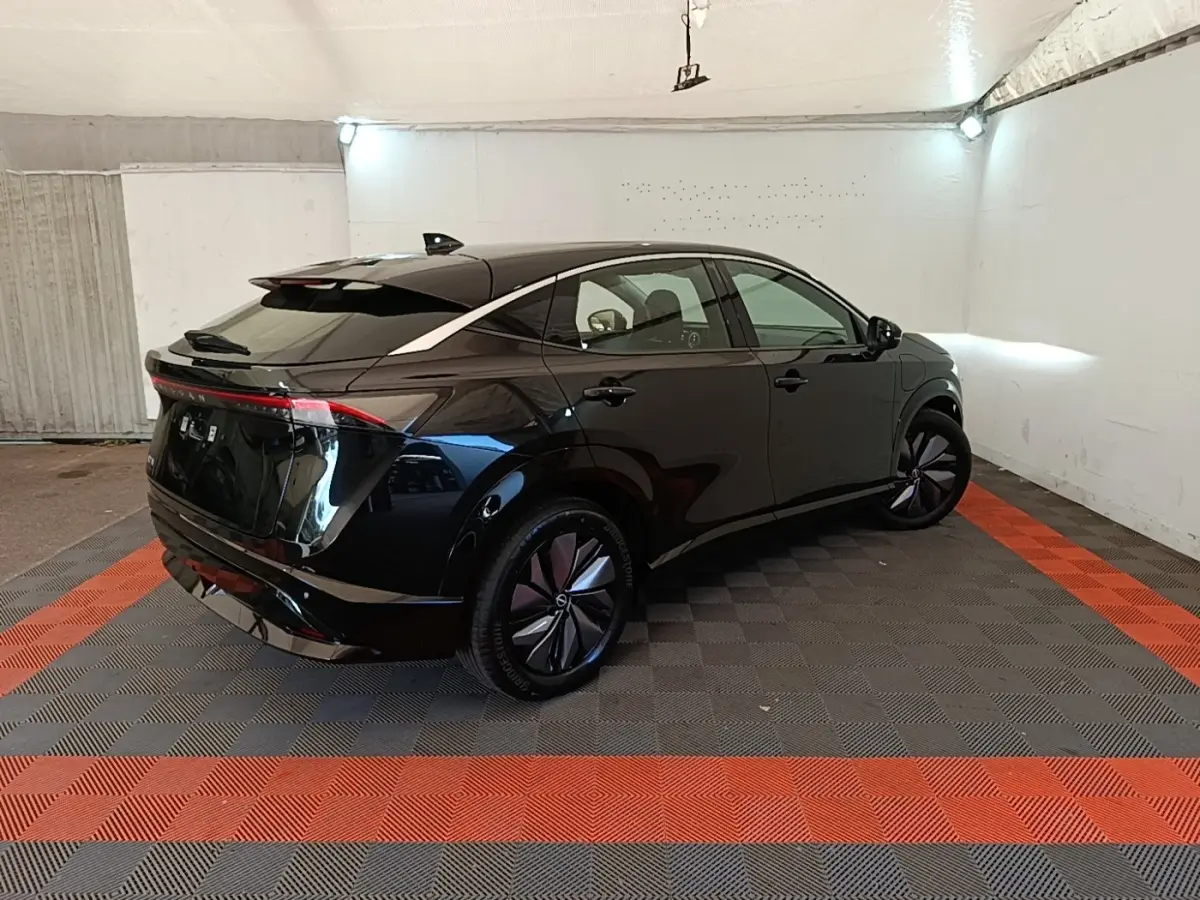 Nissan Ariya 63kWh noir en 3/4 arrière droit dans un garage, avec feux arrière continus et jantes stylisées.