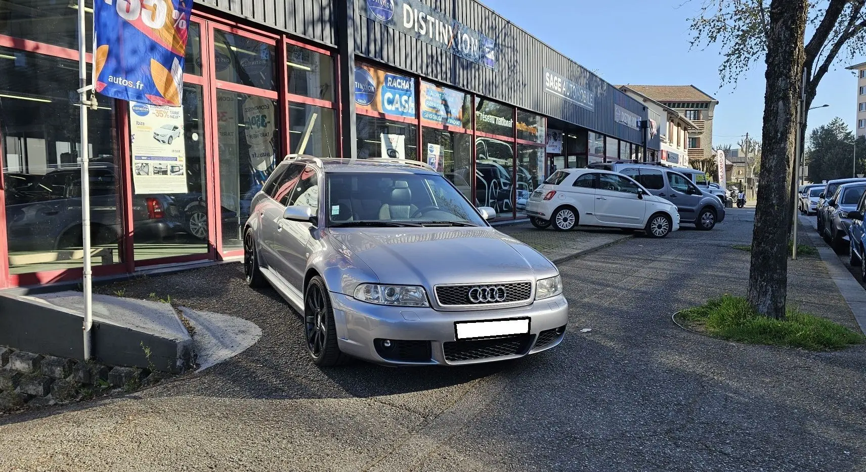 Audi RS4 Avant gris vue 3/4 avant droit, avec jantes noires et calandre distinctive, stationnée devant un atelier.