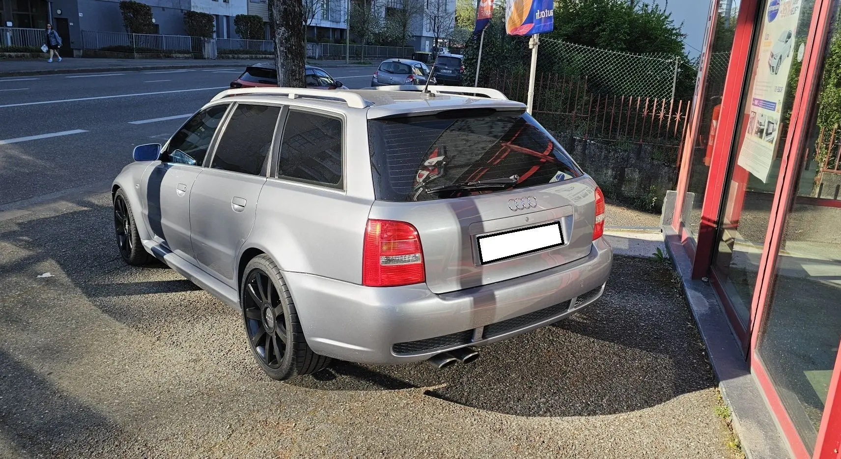 Audi RS4 Avant gris vue 3/4 arrière droit, avec jantes noires et toit ouvrant, stationnée près d'un bâtiment.