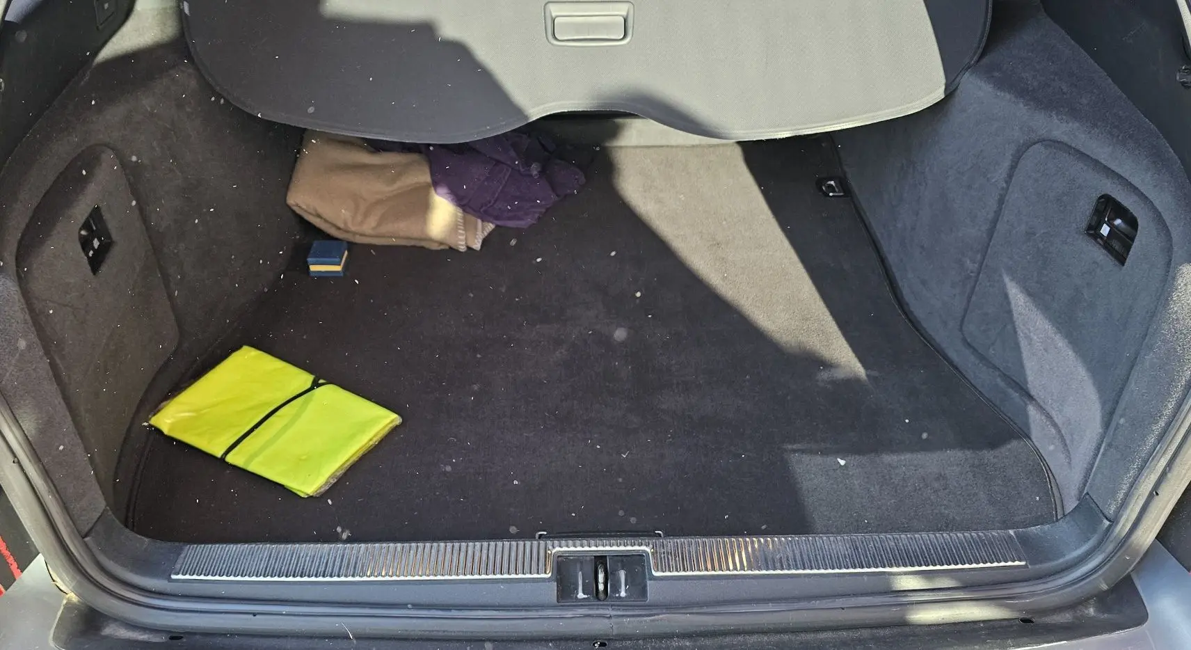 Coffre ouvert d'une Audi RS4 Avant gris 2001, montrant un tapis noir avec un gilet jaune et des vêtements pliés.