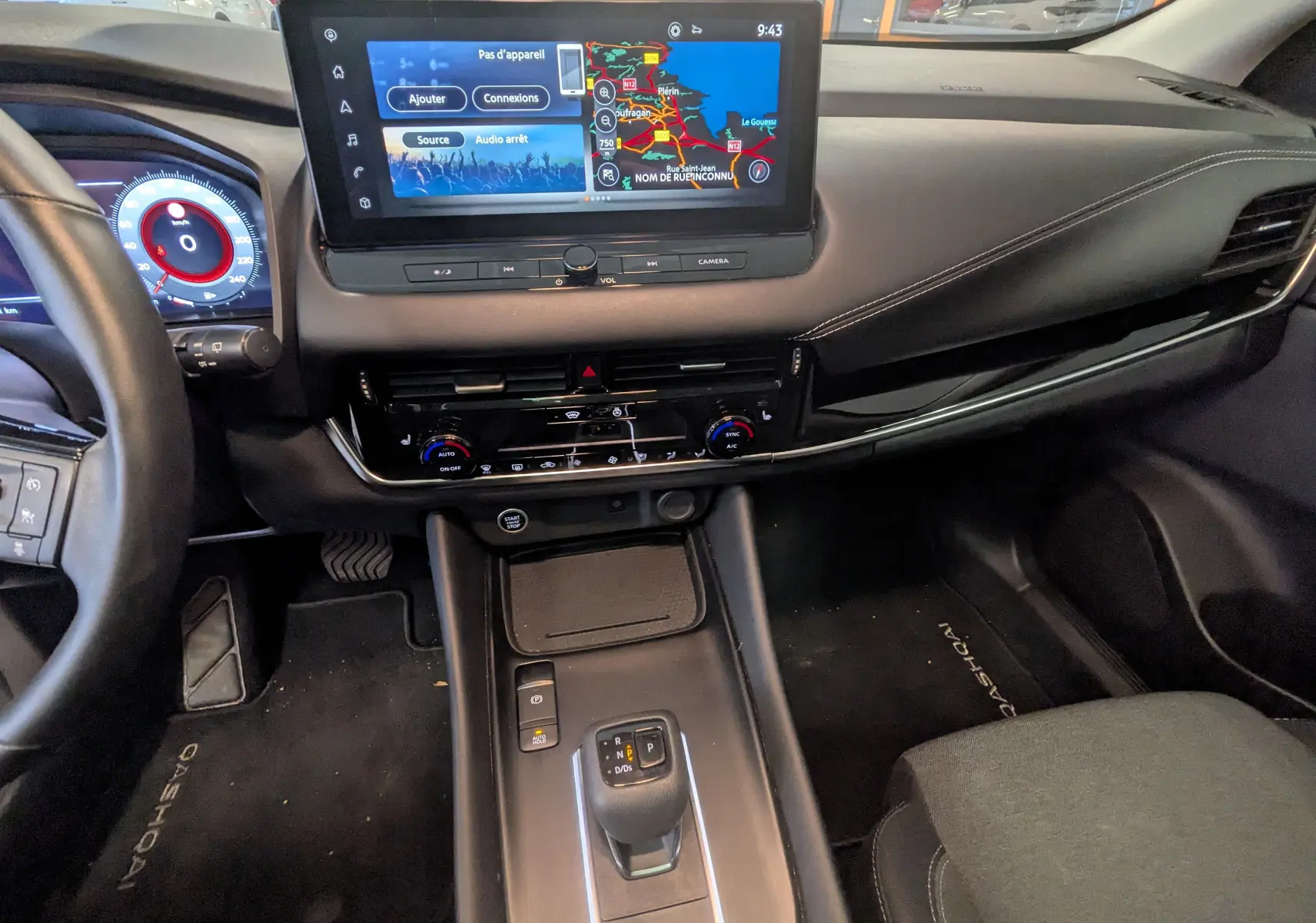Vue intérieure du tableau de bord du Nissan Qashqai 2024 blanc, avec écran tactile central et levier de vitesse automatique.