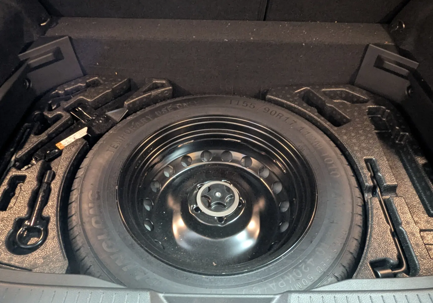 Vue rapprochée de la roue de secours noire et des outils de bord dans le coffre du Nissan Qashqai blanc 2024.