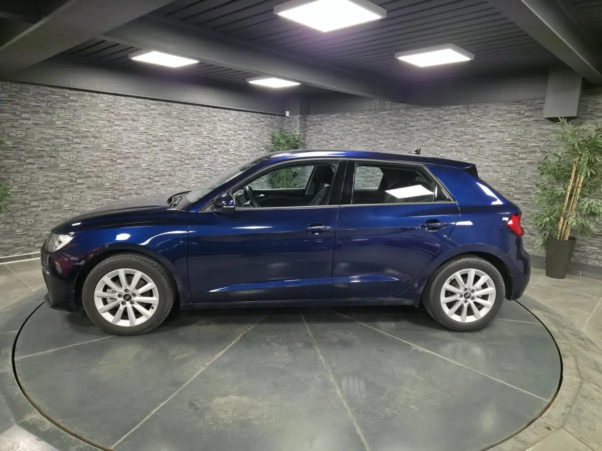 Profil côté gauche d'une Audi A1 Sportback 2024 bleu métallisé avec jantes aluminium 16 pouces dans un showroom.